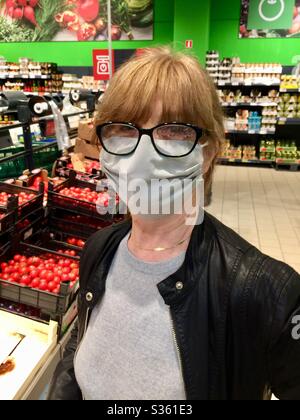 Femme âgée portant un grand masque facial et des lunettes de protection faisant ses courses au service des légumes dans un supermarché pendant la propagation du coronavirus pandémique Covid-19. Banque D'Images