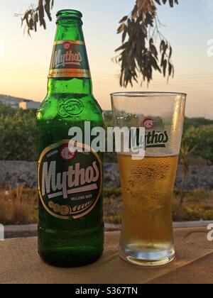 Santorini, Grèce - 20 juin 2016 : une bouteille de bière hellénique de marque Mythos et un verre sont présentés sur une table de patio de restaurant, dans une vue verticale en début de soirée. Banque D'Images