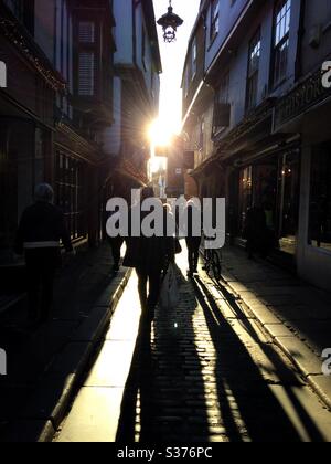 Les gens qui marchent le long d'une rue pavée vers le soleil couchant créent de longues ombres à Canterbury Royaume-Uni Banque D'Images
