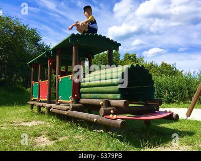 Garçon enfant enfant assis sur le train en bois de jouet à l'aire de jeux Banque D'Images