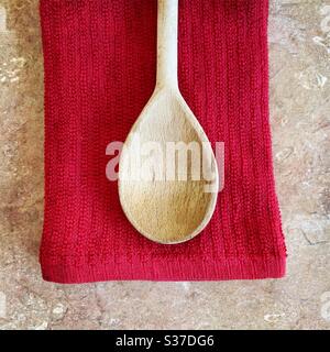 Vue rapprochée d'une cuillère en bois usée contre une torchon rouge sur le comptoir de cuisine Banque D'Images