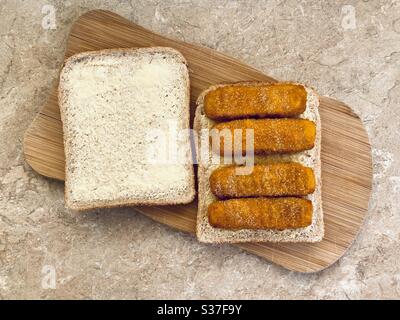 Vue rapprochée des doigts de poisson croustillants recouverts de sel et de vinaigre sur du pain beurré dans la cuisine. Préparation de sandwich avec doigts de poisson panés. Banque D'Images