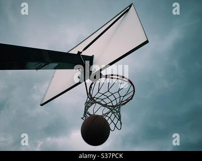 Un ballon de basket atterrit dans un panier avec un ciel spectaculaire Banque D'Images