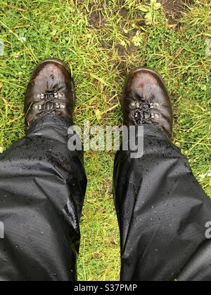 Une paire de jambes / pieds (femme) portant des bottes de marche et un pantalon imperméable, sur un sentier herbeux dans les Highlands d'Écosse, au Royaume-Uni par temps humide. Pris au milieu de l'été dans les bois près de Dornoch, Sutherland. Banque D'Images