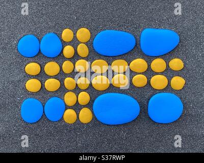 Drapeau suédois composé de galets peints en jaune et bleu sur du sable volcanique noir Banque D'Images