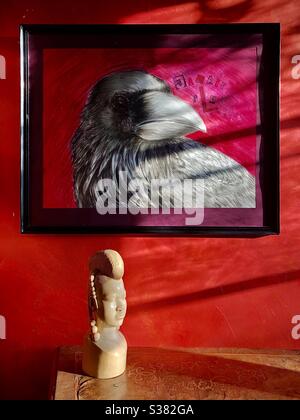 Dessin par l’artiste de la sculpture de la tête africaine et du corbeau sous la lumière du soleil contre le mur rouge. Banque D'Images