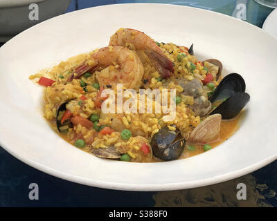 Un plat de paella, composé de crevettes, de moules, de palourdes, de pétoncles et de riz au safran dans un bouillon de fruits de mer, est présenté dans un restaurant avec vue rapprochée. Banque D'Images