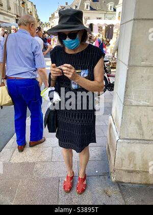 Femme dans la rue bondée portant un masque facial roulant une cigarette - France. Banque D'Images