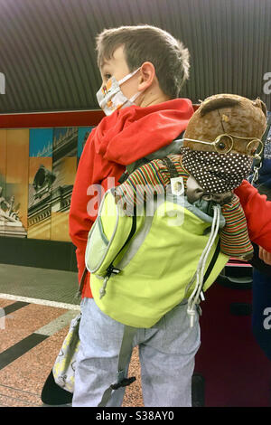 Enfant avec sac à dos et ours en peluche, tous deux portant un masque facial pendant la pandémie du coronavirus Covid-19, en attendant le train souterrain à Budapest, en Hongrie Banque D'Images