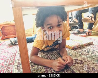 Un petit garçon jouant sous une table. Banque D'Images