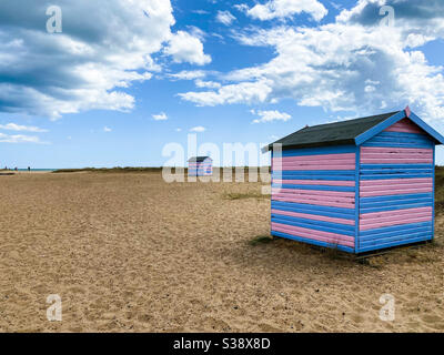 Great Yarmouth Beach Cabins en été, cabine britannique traditionnelle sur une côte est anglaise, bandes horizontales bleues et roses, ciel sans nuages, grande étendue de sable, plages britanniques Banque D'Images