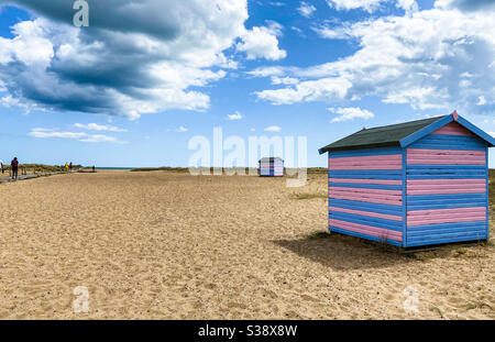 Great Yarmouth Beach Cabins en été, cabine britannique traditionnelle sur une côte est anglaise, bandes horizontales bleues et roses, ciel sans nuages, grande étendue de sable, plages britanniques Banque D'Images