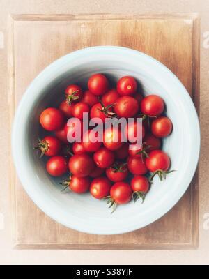 Tomates cerises dans un bol bleu sur un petit bois tableau Banque D'Images