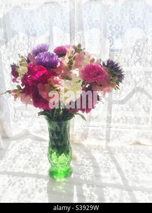 Bouquet de vivaneaux et d'asters dans un vase en verre avec un fond de fenêtre avec un rideau de dentelle. Banque D'Images