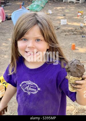 Jeune fille arrière-cour jouant à faire des cônes de glace de boue un matin d'été. Banque D'Images