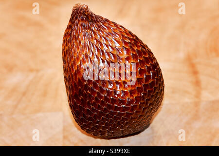 Snake fruit Salak en détail sur une assiette en bois. Vous voyez le grain fin et la structure de la peau de ce fruit mûr, qui ressemble à un serpent Banque D'Images