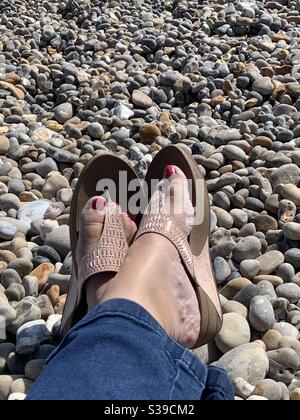 Pieds dans des tongs sur une plage de galets Banque D'Images