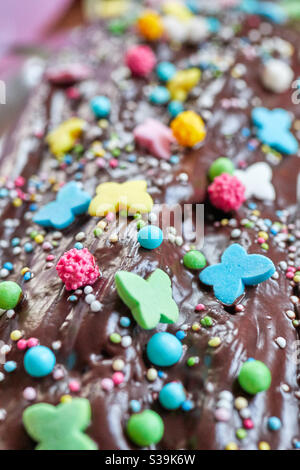 une douce et savoureuse décoration colorée avec des papillons et des boules de sucre sur le glaçage brun brillant d'un gâteau d'anniversaire au chocolat. Cette photo de détail est délicieuse Banque D'Images