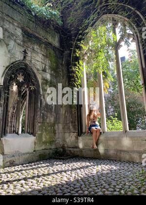 Femme assise dans une arche de pierre avec des plantes et le soleil brillant par Banque D'Images