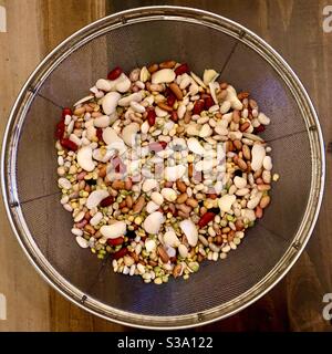 Une variété de 15 haricots secs dans une passoire circulaire sur une table en bois. Banque D'Images