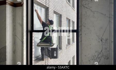 LOS ANGELES, CA, JUL 2020: Le nettoyeur de fenêtres fonctionne sur les hautes fenêtres d'un siège attaché à un harnais de corde, à l'extérieur d'un bâtiment historique dans le centre-ville Banque D'Images