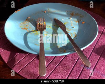 Une assiette bleue sur un napperon violet, après qu'un friture a été mangé Banque D'Images