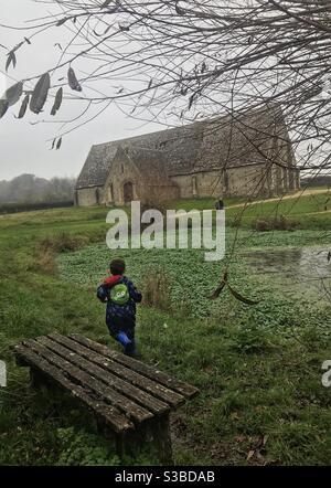 Enfant en train de courir avec la tithe Barn en arrière-plan Banque D'Images