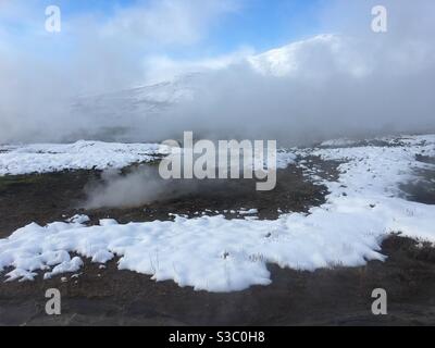 La vapeur s'élève des évents géothermiques dans la neige d'hiver avec les montagnes En arrière-plan à l'Islande Banque D'Images