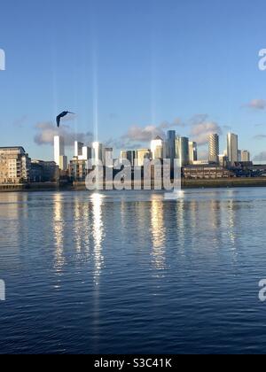 La Tamise coule à basse vitesse tandis que le soleil se couche sur Londres. De l'autre côté de la rivière Canary Wharf peut être vu derrière des bâtiments privés qui se reflètent dans l'eau tandis qu'un moulus s'élancera le long de la rive de la rivière Greenwich. Banque D'Images