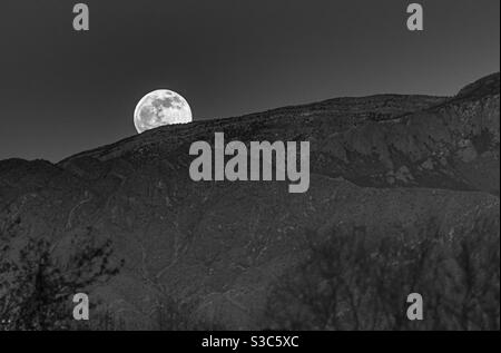 La pleine lune s'élève au-dessus des montagnes Sandia à Albuquerque, Nouveau-Mexique. Banque D'Images