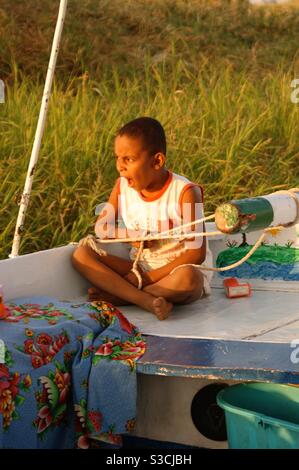 Le jeune garçon égyptien est assis sur le pont de felucca sur le Nil, tirant les cordes de navigation tout en bâillant au coucher du soleil Banque D'Images