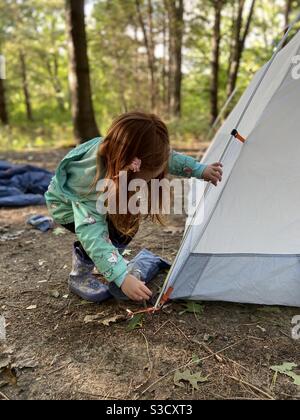 Petite fille douce aidant à mettre en place une tente à la camping tout en camping familial dans la forêt à l'automne dans un terrain de camping paisible Banque D'Images