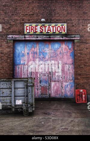 L'entrée et la porte d'un très vieux et déserté caserne de pompiers avec panneau et porte colorée Banque D'Images