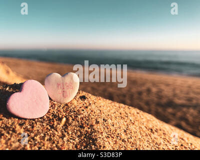 Deux friandises de Saint-Valentin dans le sable sur une plage ensoleillée. L'un des bonbons a les mots manquent vous imprimé dessus. Banque D'Images