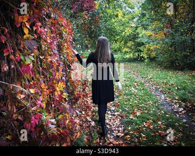 Vue arrière de la femme en robe noire debout près du portes d'un jardin avec des feuilles de lierre rouge et jaune Banque D'Images