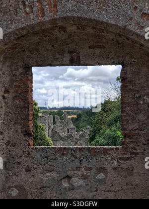 Vue à travers une fenêtre du palais du Prieuré de Castle Acre, à travers les ruines prieuré et la campagne de Norfolk au-delà. Près de Swaffham, Norfolk, Angleterre. Banque D'Images