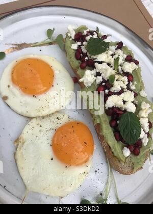 Avocat crémeux sur pain de levain recouvert de graines de grenade et fromage féta émietté et deux œufs frits de taille moyenne Banque D'Images