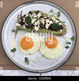 Avocat crémeux sur pain de levain recouvert de graines de grenade et fromage féta émietté et deux œufs frits de taille moyenne Banque D'Images