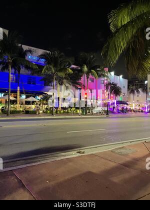 Des néons roses et bleus illuminent les rues de la célèbre Collins Avenue du sud de Miami Beach, en Floride, aux États-Unis, avec des restaurants, des boutiques, des restaurants en plein air, des palmiers et des gens qui regardent Banque D'Images