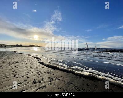 Belle vue panoramique du coucher de soleil sur l'océan depuis la plage de Prestwick, Ayrshire, Écosse sur Firth of Clyde, côte ouest avec deux yachts naviguant dans la mer. Banque D'Images