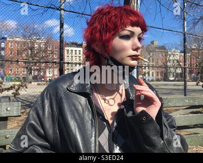 Punk style adolescent avec des cheveux rouges fumer la cigarette dans le parc de la place Tompkins dans le côté inférieur est, manhattan New York City. Banque D'Images