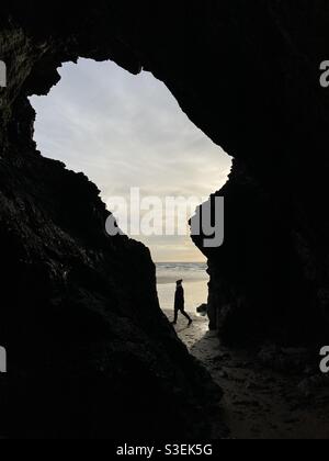 Pendant que la femme passe devant une grotte de la mer sur la plage de Perranporth, dans les Cornouailles Banque D'Images