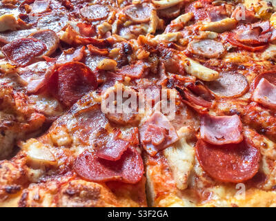 Vue rapprochée d'une pizza de fête de viande avec bacon, jambon, fromage, tomate et pepperoni pour la garniture. Banque D'Images