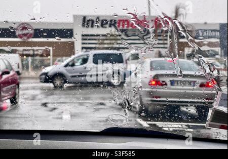 Pluie sur le pare-brise d'une voiture garée devant un supermarché français, près de Montpellier, Occitanie, sud de la France Banque D'Images