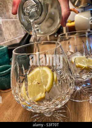 Fabrication de gin tonic- remplir des verres coupés avec des tranches de citron et les glaçons avec du gin Banque D'Images