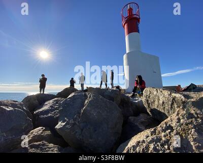 Touristes se tenant au-dessus d'un brise-lames près d'un phare à Palavas les Flots près de Carnon Plage et Montpellier, Occitanie, sud de la France Banque D'Images