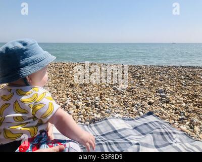 Un bébé est assis sur une plage de galets qui donne sur la mer, à Eastbourne, en Grande-Bretagne. Banque D'Images