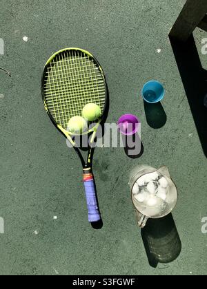 Vue à vol d'oiseau des raquettes de tennis sur un court de tennis avec des balles de tennis le long d'un pichet de glace froide eau et quelques tasses sur un chaud ensoleillé jour Banque D'Images