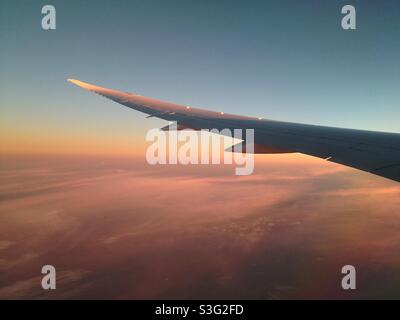 L'aile d'un Boeing 787 Dreamliner survolant l'océan Atlantique au coucher du soleil.Nuages aux couleurs chaudes. Banque D'Images