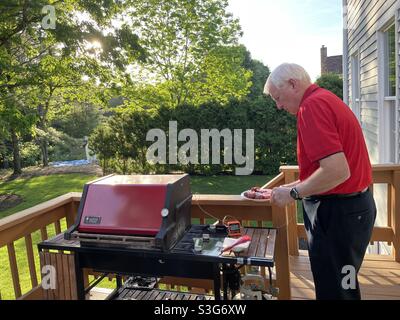 L'homme senior prépare la viande à griller sur son barbecue Weber classique sur sa terrasse arrière de banlieue, aux États-Unis Banque D'Images